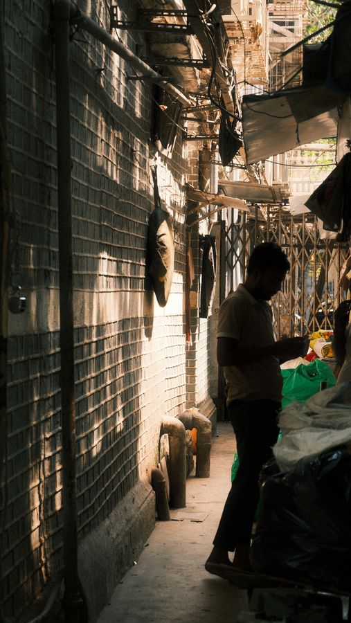 A man standing in a narrow shaded lane beside a tiled wall