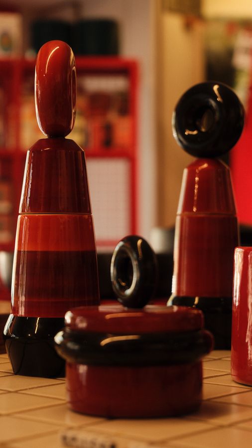 Red and black lacquered spice mills and a jar on a tiled counter