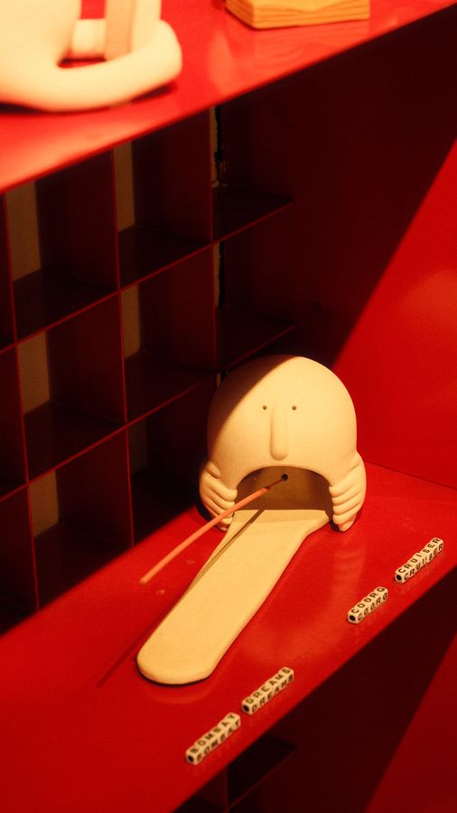A white ceramic face with a long flat nose resting on a red shelf