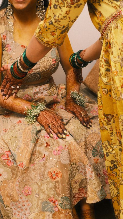 Hennaed bridal hands with green and gold bangles resting on an embroidered lehenga